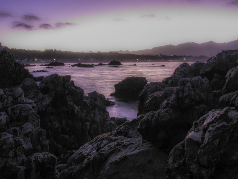 Rocks leading out to a lake surrounded by mountains and a purple sky in New Zealand