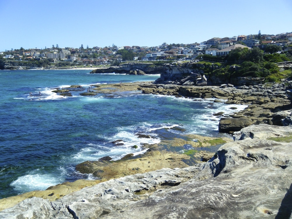 Rocks meet the ocean on the coastal walk from Bondi Beach to Coogee Beach in Sydney as the city lies in the background
