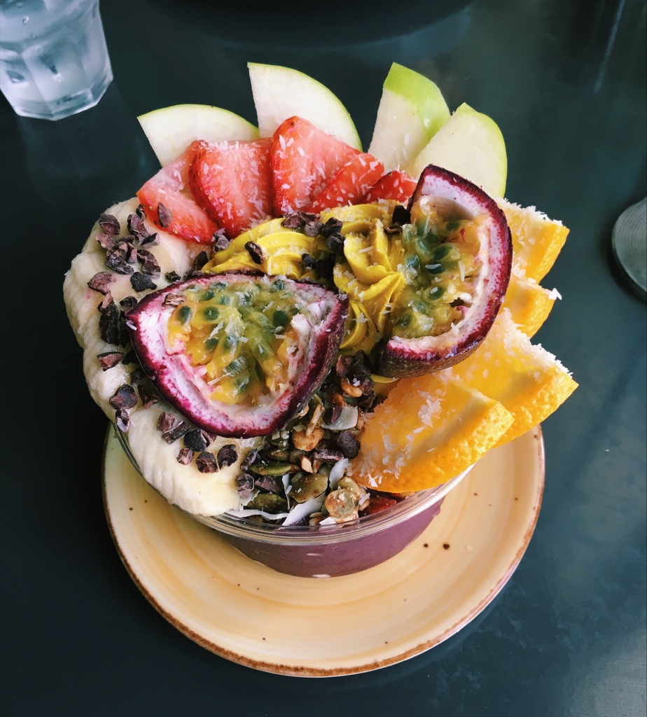 Acai bowl topped with fresh fruit, granola and shaved coconut sits on a black countertop