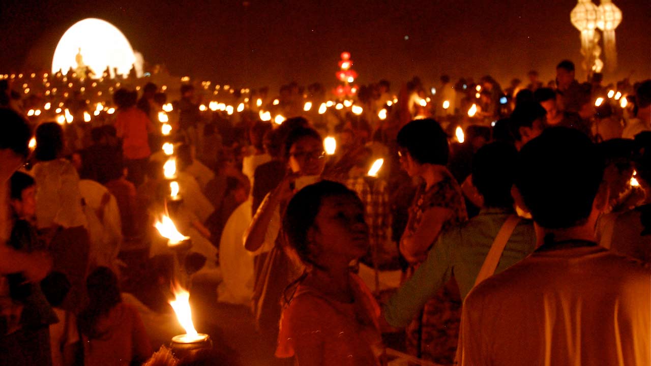 Crowds of people hold lit candles for an evening ceremony in Chiang Mai