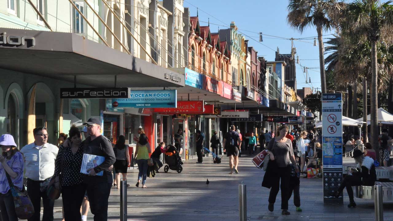 Pedestrians walk along the main row of shops in downtown Manly, Australia