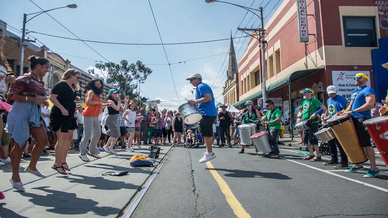 A man jumps in the air while playing a drum and hyping up the crowd at a street festival in Melbourne