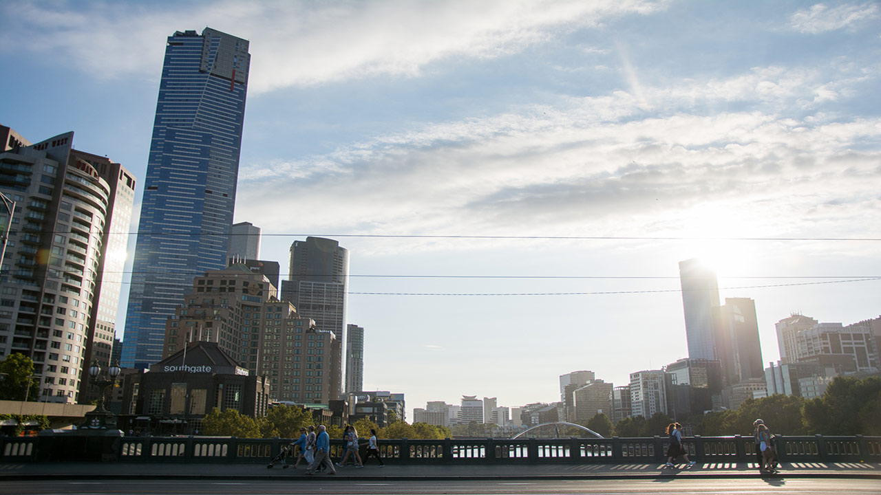 People walk along a bridge in downtown Melbourne that connects two city neighbourhoods at dusk