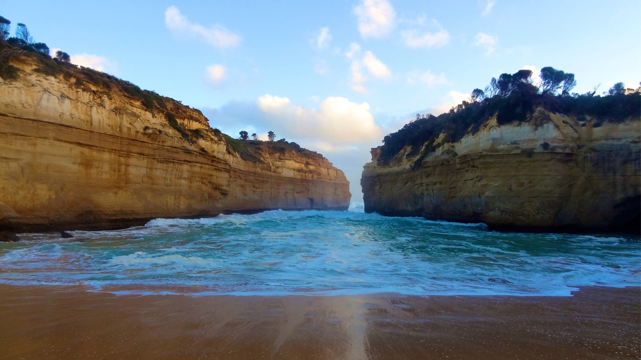 Waves crash onto the shore, set between two cliffs jutting from the ocean