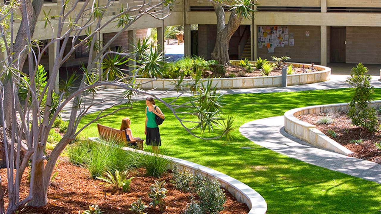Two women chatting in a grassy quad on Murdoch University's campus in Perth, Australia
