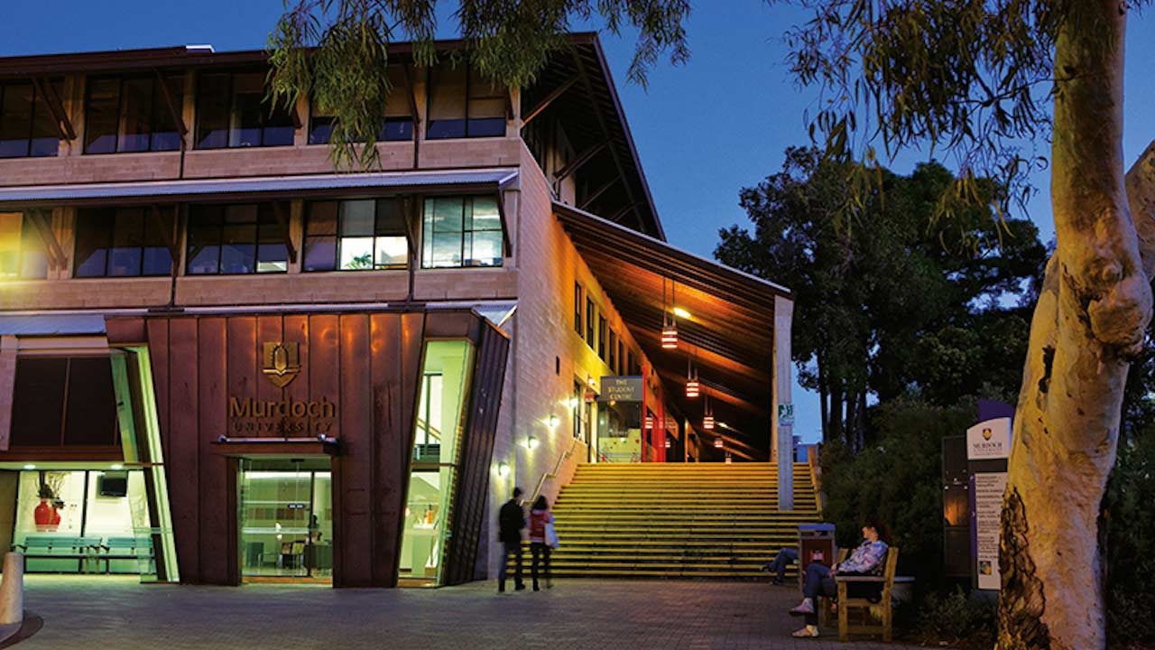 Two people walk towards an illuminated building on Murdoch University's campus in Perth, Australia