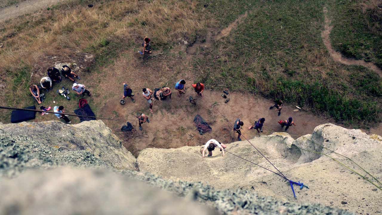 Students stand at the base of a craig as one person climbs up the rock formation