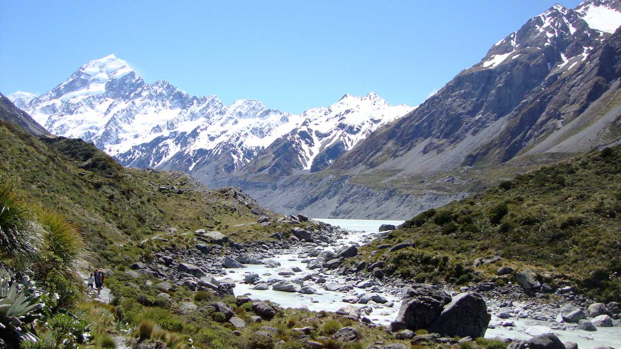 A rocky stream surrounded by grassy peaks leading to snow capped mountains