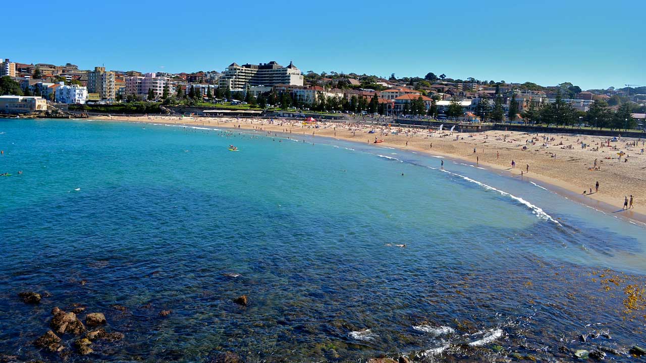 Multiple shades of blue ocean break on the sandy shore in Sydney, Australia