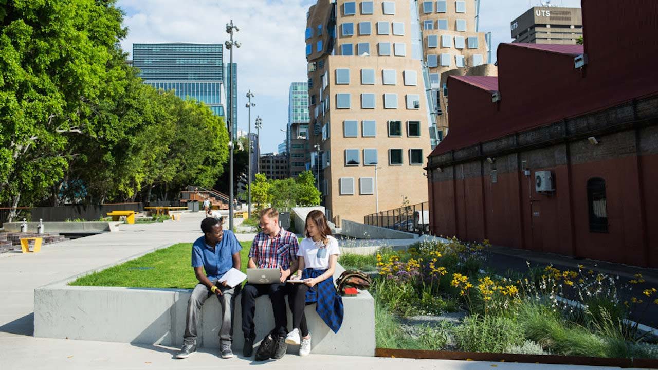 Three people sit chatting on a bench on UTS's campus