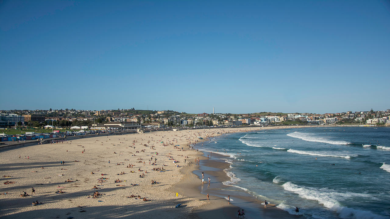 A landscape view of Bondi Beach in Sydney, as the waves come into the shore and many people lay about