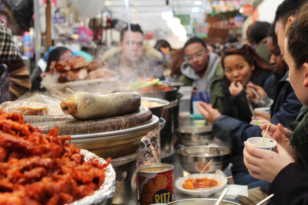 Group sitting around a counter having a meal at Gwangjang Market